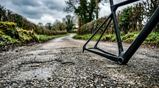 Carbon fiber bicycle frame positioned against weathered British tarmac background, subtle road texture detail