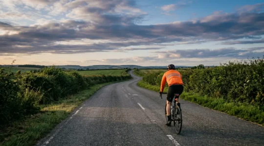 Solo cyclist on rural road with rear-mounted radar device under dramatic sky
