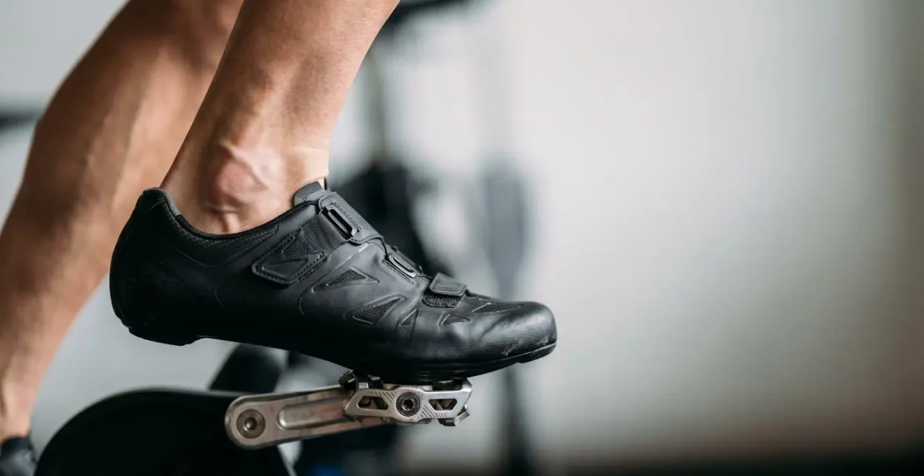 Side-view close-up of cyclist's foot in carbon shoe on pedal showing proper cleat alignment relative to metatarsal heads