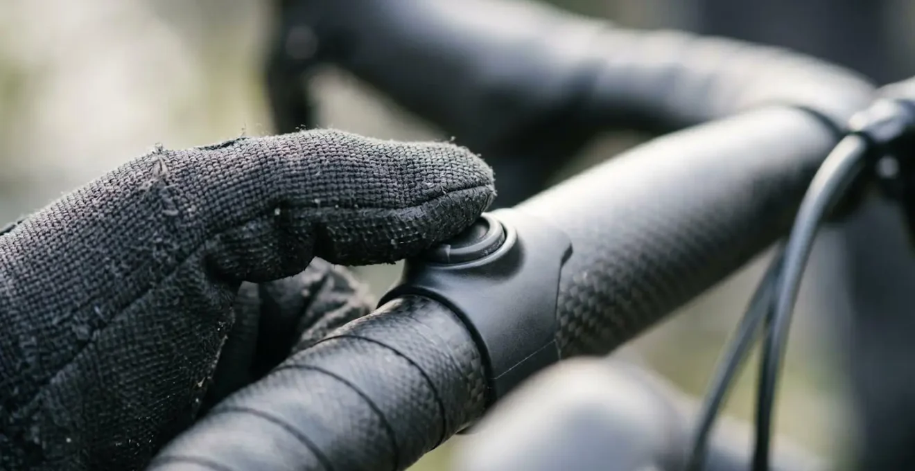 Macro detail of cyclist's gloved finger pressing electronic shifter button on handlebar