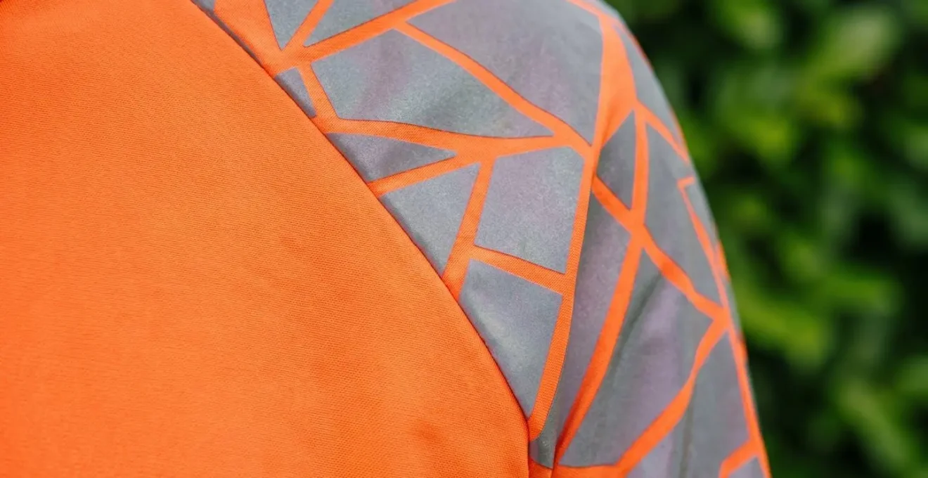 Close-up detail of modern cycling jacket with bold geometric pattern-breaking reflective design against natural green hedge background